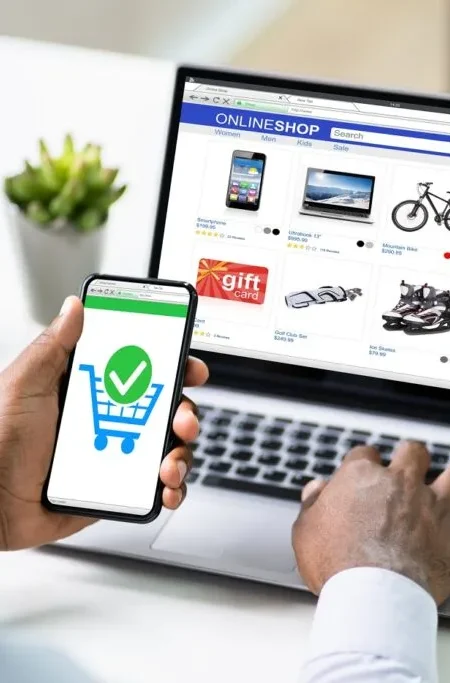 A modern laptop on a desk showing an online store homepage with products and a shopping cart