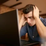 frustrated freelancer holding head while working on laptop