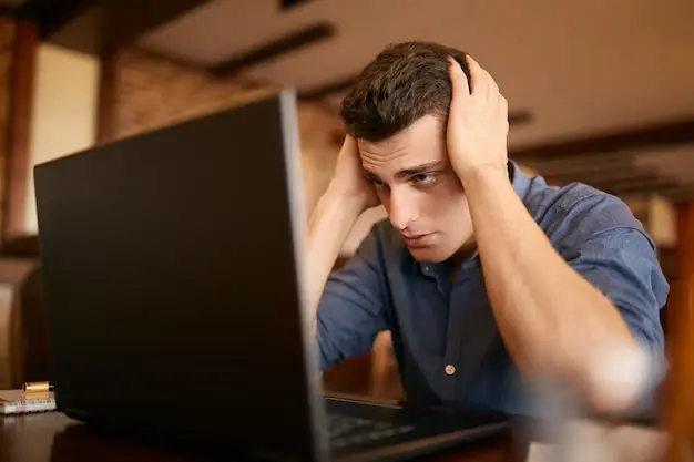 frustrated freelancer holding head while working on laptop